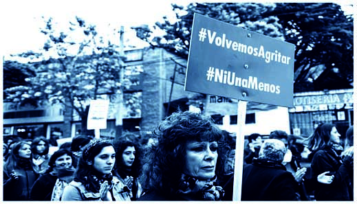 Foto einer Frauen Demonstration in Chile. Eine Frau im Vordergrund hält ein Schild mit dem Slogan Volvemos Agritar und NiUna Menos hoch